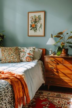 a bedroom with blue walls and an orange blanket on the bed next to a dresser