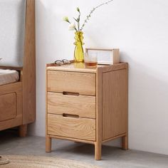 a wooden nightstand with two drawers next to a bed and a yellow vase filled with flowers