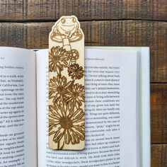 an open book with a wooden bookmark on top of it and flowers in the middle