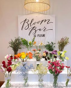 a table topped with lots of vases filled with flowers next to a sign that says bloom bar