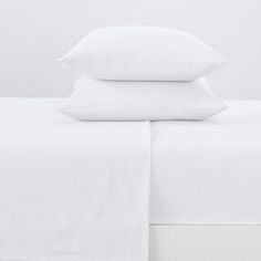 three white pillows stacked on top of each other in front of a plain white bed