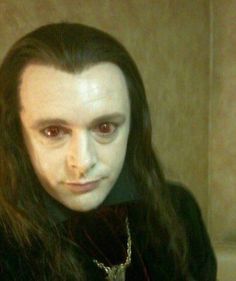 a man with long hair and white makeup looks at the camera while wearing a mask