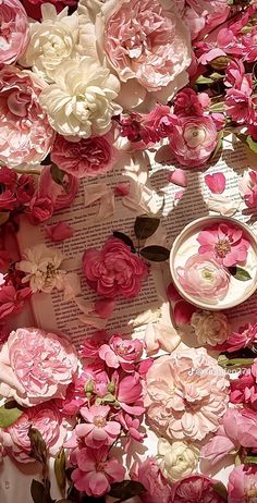 pink and white flowers on top of an open book with a plate in the middle