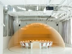 an empty room with white chairs and orange lights on the ceiling in front of a round table