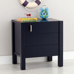 a night stand with a clock and books on it in front of a wall mounted life preserver