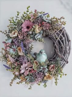 a wreath with flowers and a bird sitting on top of it, against a white wall