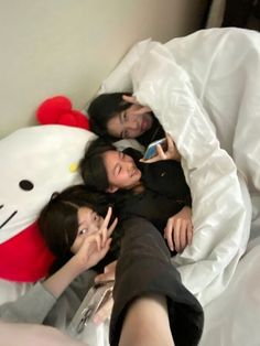 three women laying in bed with a hello kitty pillow