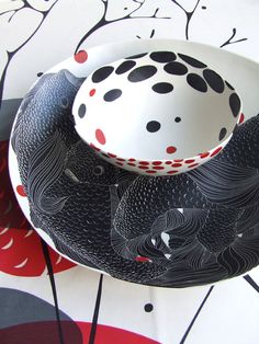 a black and white bowl sitting on top of a table next to a plate with red dots