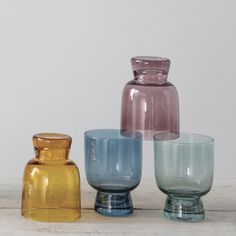 three different colored glass vases sitting next to each other on a white table top