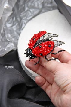 a hand holding a red and black insect brooch