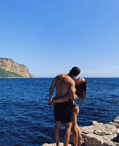 a man and woman are standing on rocks by the water