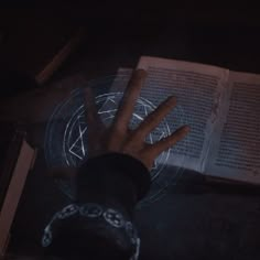 a person's hand on top of an open book in front of a candle