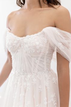 a woman in a white dress is wearing an off the shoulder dress with flowers on it