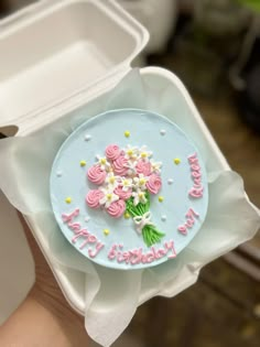 a person holding a birthday cake with flowers on it