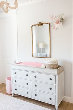 a baby's room with a dresser, mirror and pink blanket on the floor