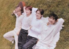 four young men laying on the grass with their arms around each other