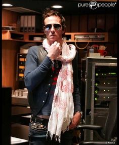 a man wearing sunglasses and a scarf standing in front of a sound mixing equipment with his hand on his mouth