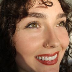 a close up of a woman with curly hair and piercing on her nose smiling at the camera