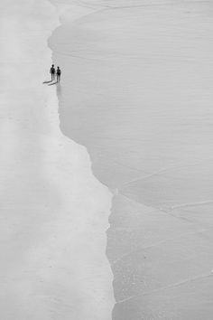 two people are walking along the beach in black and white