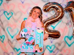 a woman holding up a large number sign in front of a backdrop with hearts and balloons