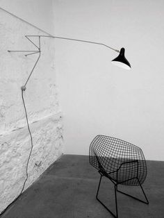 a black and white photo of a chair next to a wall with a lamp on it