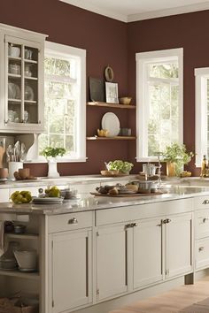 a kitchen with white cabinets and lots of dishes on top of the counter tops in front of two windows