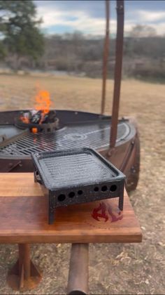 a grill sitting on top of a wooden table next to an open fire pit with flames