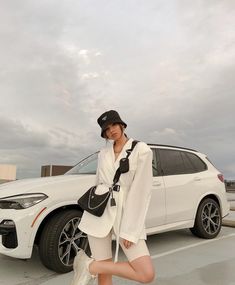 a woman is posing in front of a white bmw suv with her legs spread out