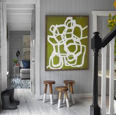 a painting hangs on the wall above two stools in front of an entry way