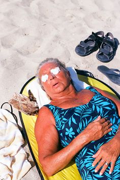 an older woman laying on top of a yellow and black beach bag next to flip flops