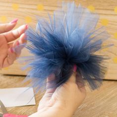 a person is holding a piece of blue tulle in their hand and scissors are next to it