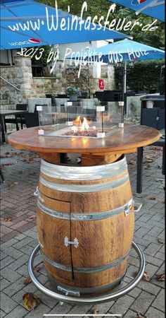 a wooden barrel sitting on top of a table next to a fire pit with an umbrella over it