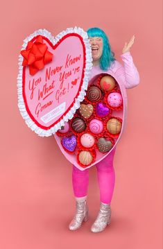 a woman holding a heart shaped box filled with lots of chocolates on top of a pink background