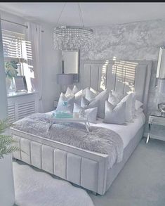 a bed with white sheets and pillows in a bedroom next to a window filled with windows