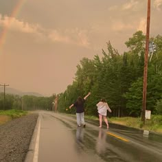 two people are walking down the road with their arms in the air and one person is holding an umbrella