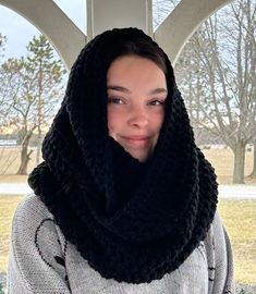 a woman wearing a black scarf over her head and looking at the camera while standing in front of a window