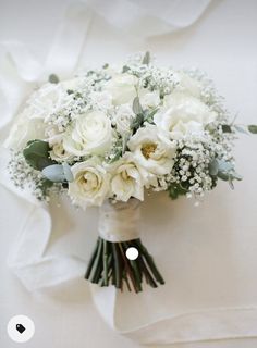 a bridal bouquet with white roses and baby's breath on a white cloth