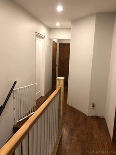 an empty hallway with wood floors and white walls, along with a wooden banister