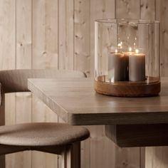 two lit candles sit in a glass container on a table next to a wooden chair