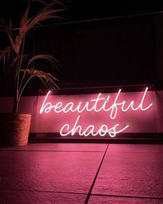 a neon sign that says beautiful chaos on the side of a building in front of a potted plant