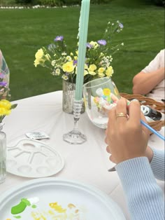 a woman is painting flowers in vases on a table with plates and candles at an outdoor event