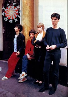 four people standing in front of a building with a clock on the wall behind them