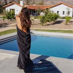 a woman standing in front of a swimming pool wearing a black towel over her back