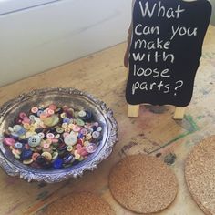 a bowl filled with buttons next to two cork coasters on top of a table