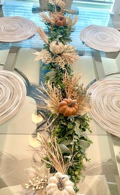 a glass table topped with white pumpkins and greenery