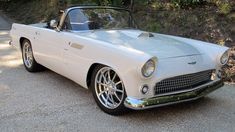 an old white convertible car parked on the side of a road with trees in the background