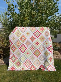 a quilt is laying on the grass in front of a tree