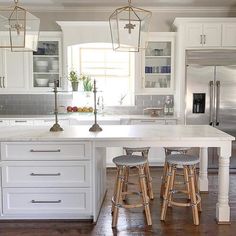 a kitchen with white cabinets and wooden stools next to an island in the middle