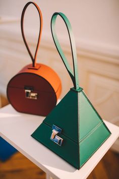 two small purses sitting on top of a white table next to an orange and green bag