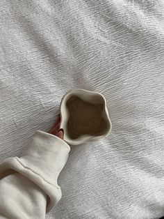 a person's hand holding an empty bowl on top of a bed